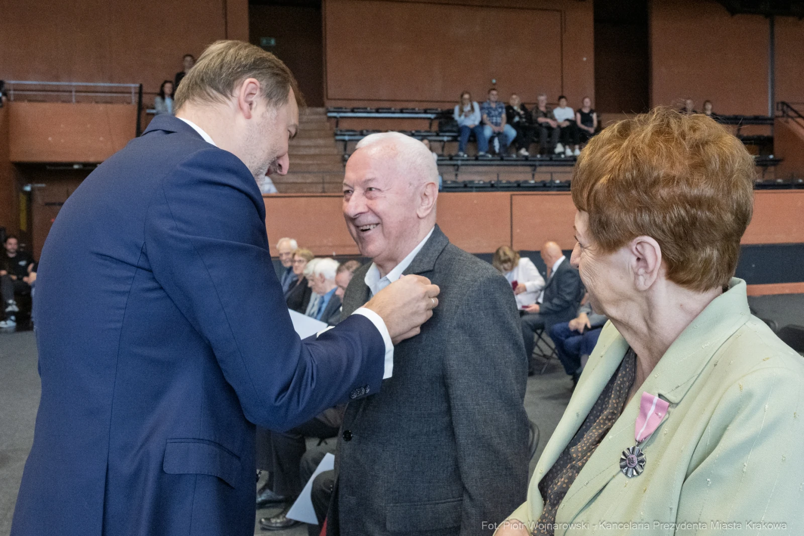 Mężczyzna otrzymuje odznaczenie, obok stoi uśmiechająca się kobieta.  Autor: Piotr Wojnarowski