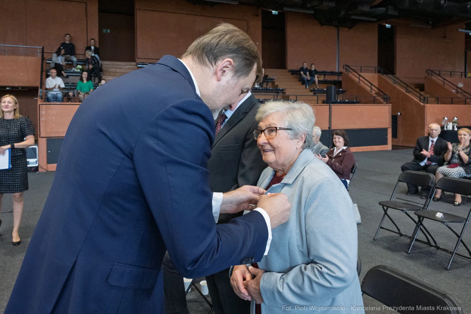 Wręczenie odznaczenia starszej kobiecie przez mężczyznę w garniturze podczas uroczystości.  Autor: Piotr Wojnarowski