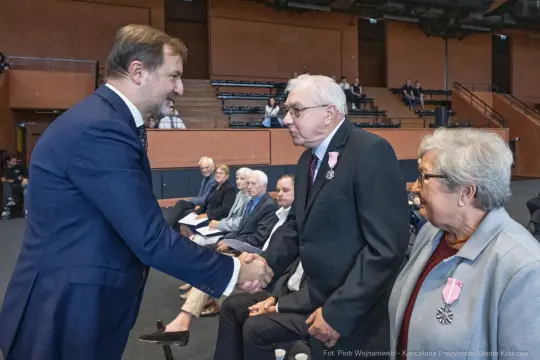 Uroczystość wręczenia odznaczeń, mężczyzna w garniturze wita odznaczonego mężczyznę.