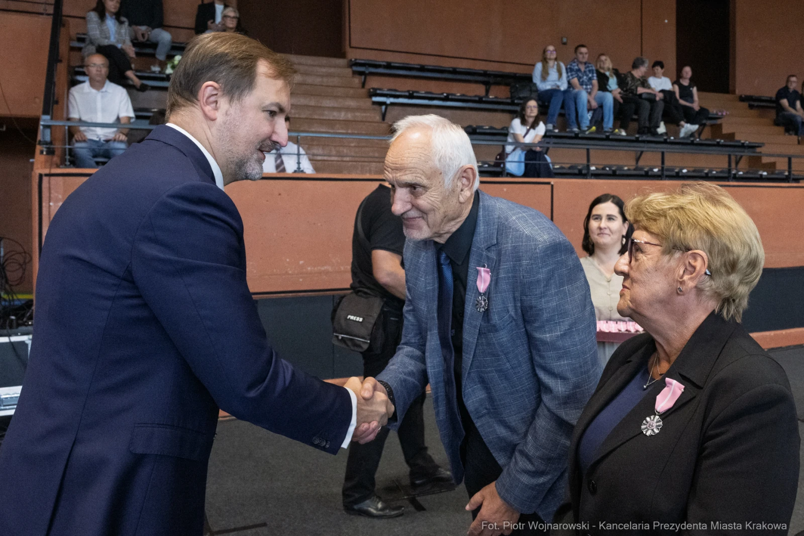 Mężczyzna w garniturze wita się z starszym mężczyzną i kobietą w eleganckich strojach.  Autor: Piotr Wojnarowski