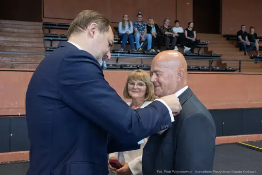 Uroczystość wręczenia odznaczenia mężczyźnie przez oficjela, w tle widownia.