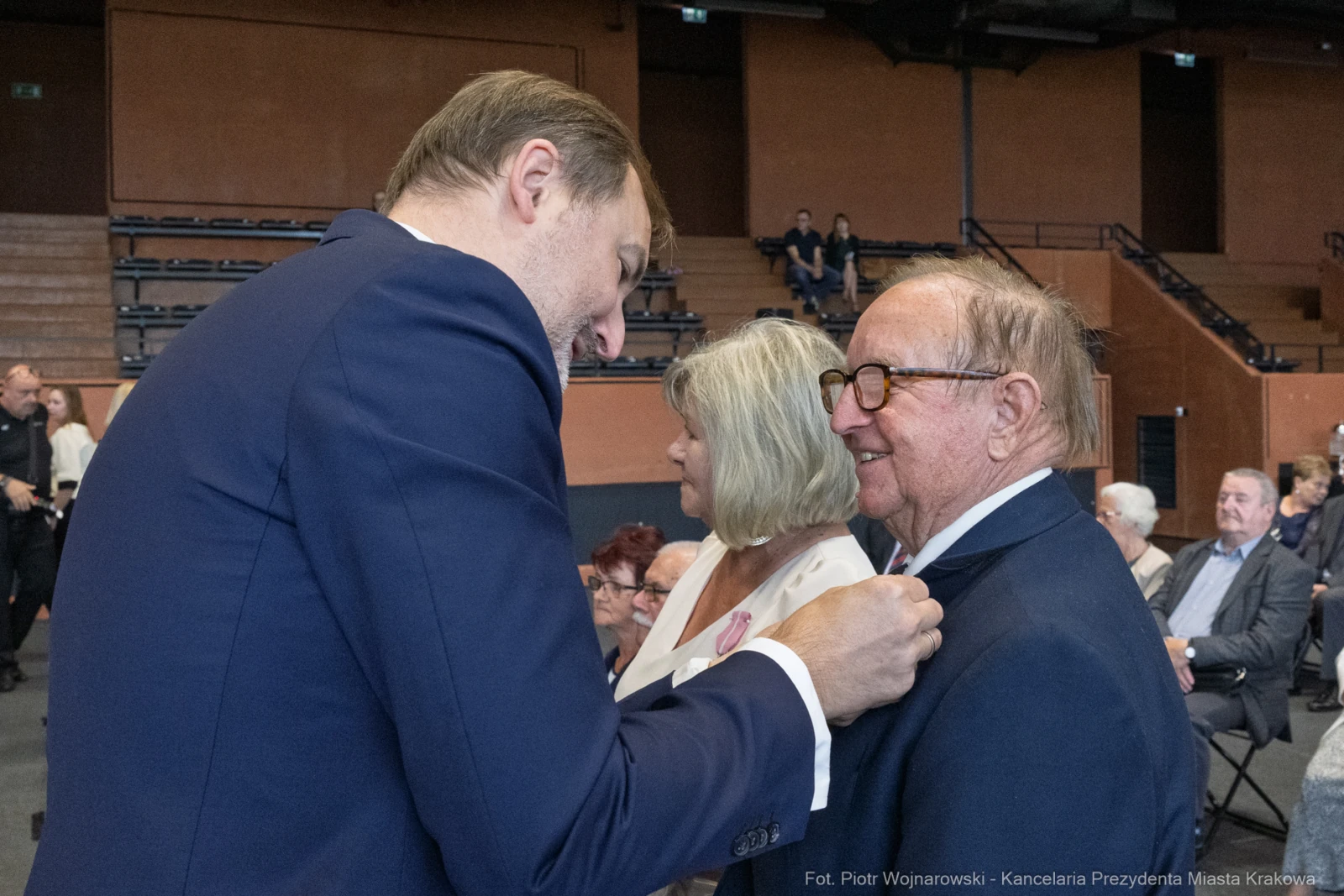 Mężczyzna przypina odznaczenie starszemu mężczyźnie w towarzystwie kobiety.  Autor: Piotr Wojnarowski