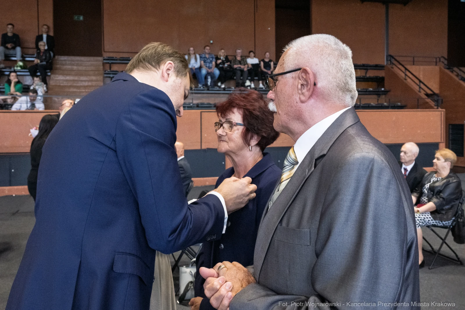 Wręczenie odznaczenia osobie starszej przez mężczyznę w garniturze. W tle widownia.  Autor: Piotr Wojnarowski