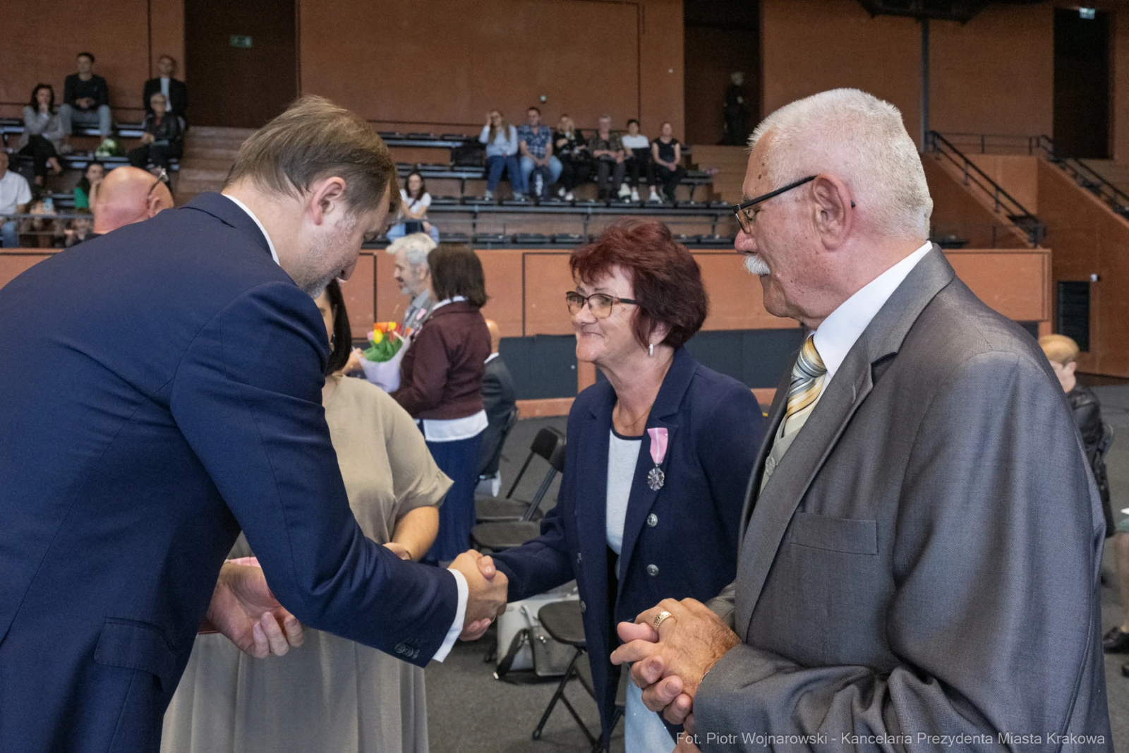 Uścisk dłoni między mężczyzną a kobietą w formalnej atmosferze. W tle widoczna publiczność.  Autor: Piotr Wojnarowski