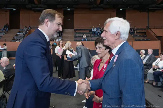 Uroczystość wręczenia odznaczeń, mężczyzna w garniturze podaje rękę innemu mężczyźnie.
