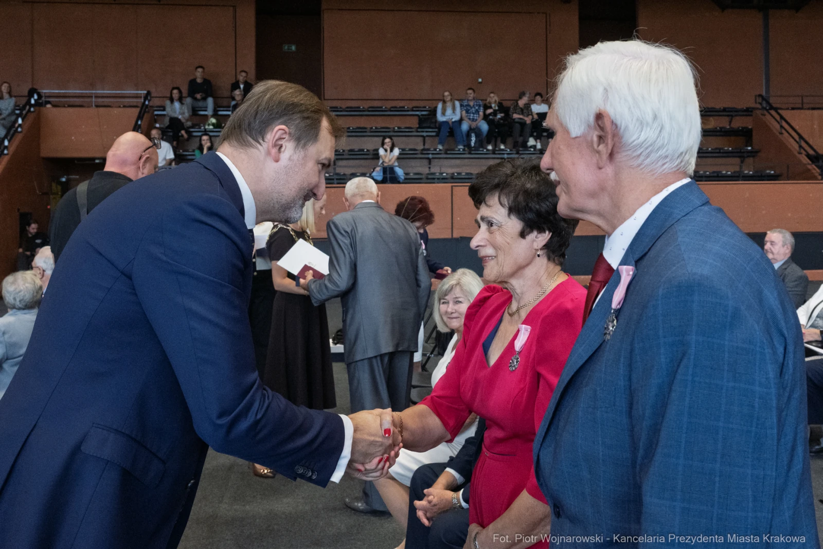 Uścisk dłoni między mężczyzną a kobietą w eleganckich strojach, w tle inni goście.  Autor: Piotr Wojnarowski