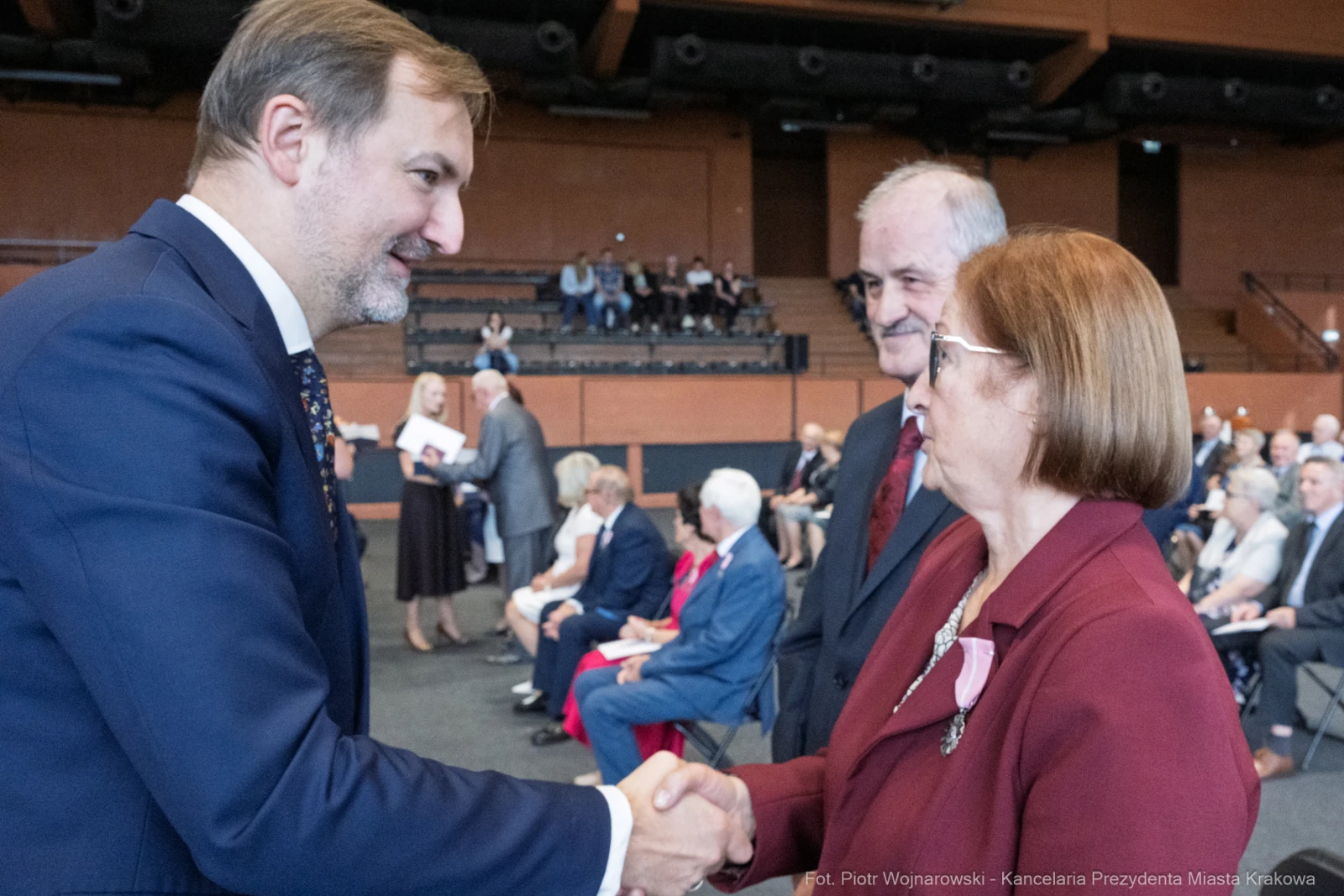 Spotkanie dwóch osób podczas uroczystości, uścisk dłoni i rozmowa. W tle widoczna publiczność.  Autor: Piotr Wojnarowski