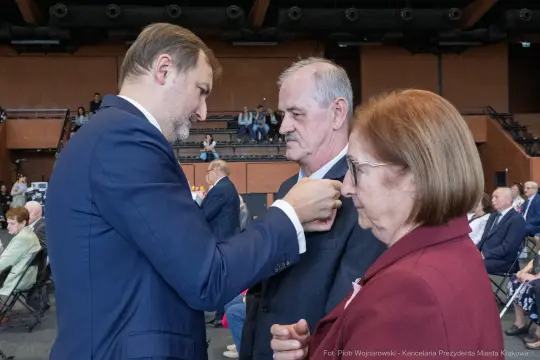 Wręczenie odznaczeń przez mężczyznę starszym parze podczas uroczystości.