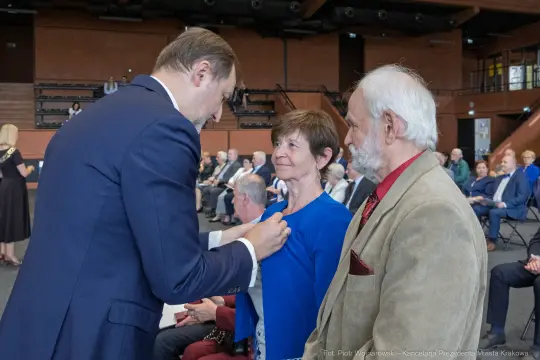 Wręczenie odznaczenia kobiecie przez mężczyznę w formalnym otoczeniu.