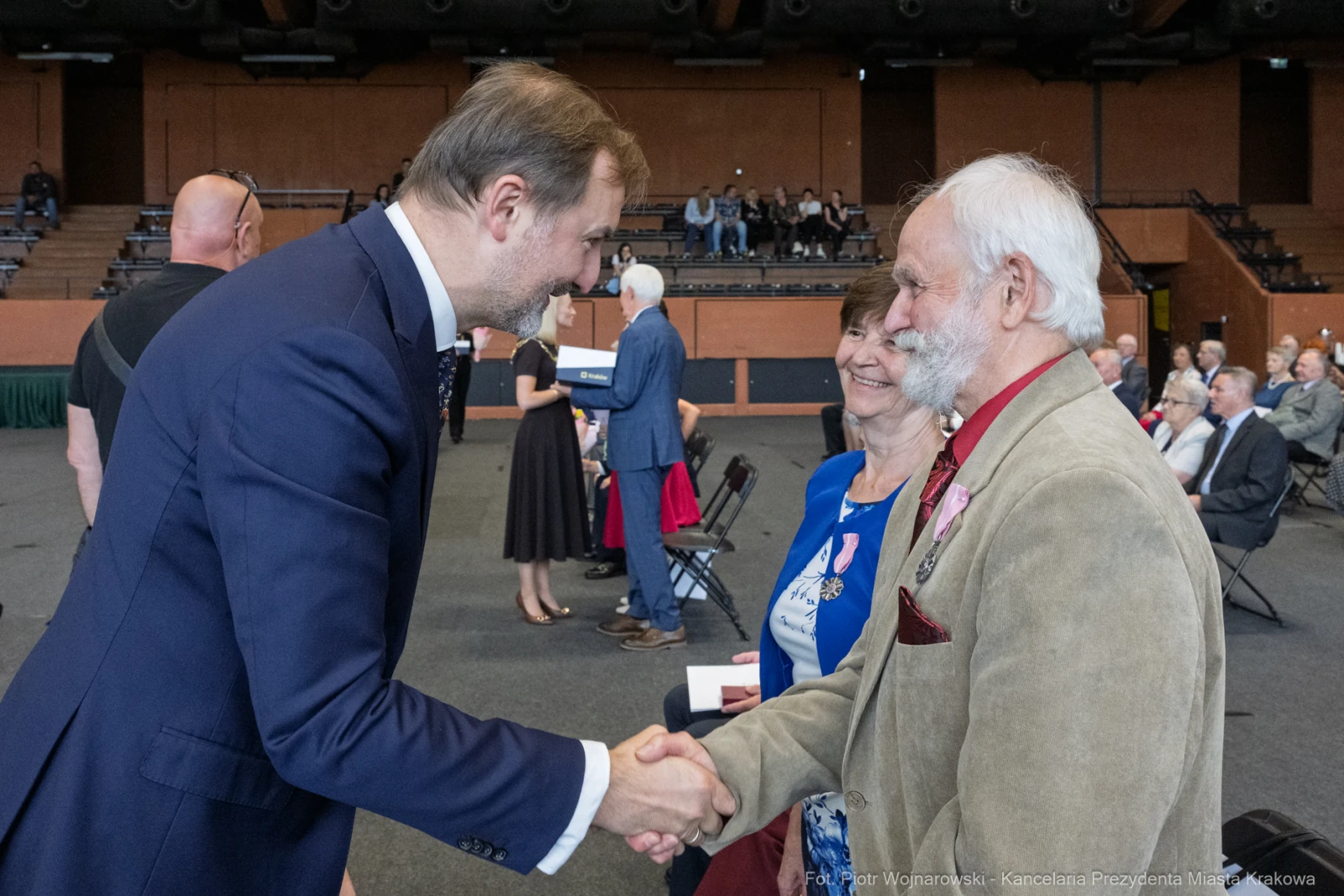 Uścisk dłoni podczas uroczystości, w tle zgromadzenie osób w formalnych strojach.  Autor: Piotr Wojnarowski