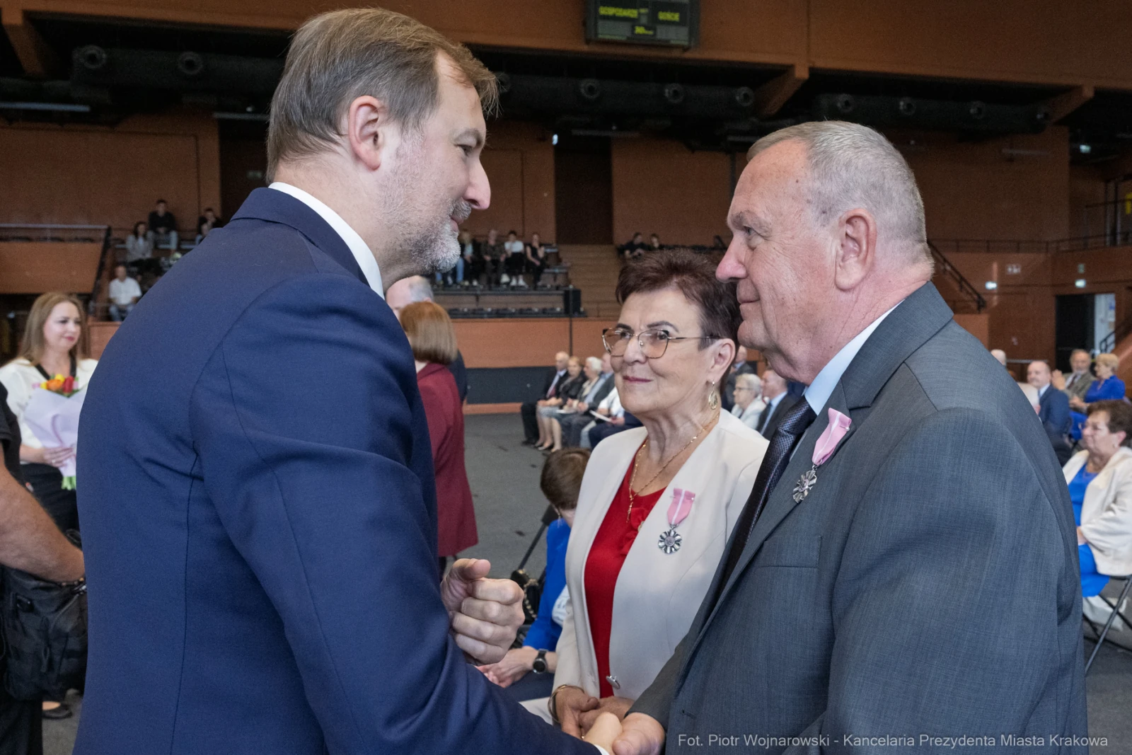 Spotkanie dwóch mężczyzn i kobiety w eleganckich strojach, w tle widoczna publiczność.  Autor: Piotr Wojnarowski