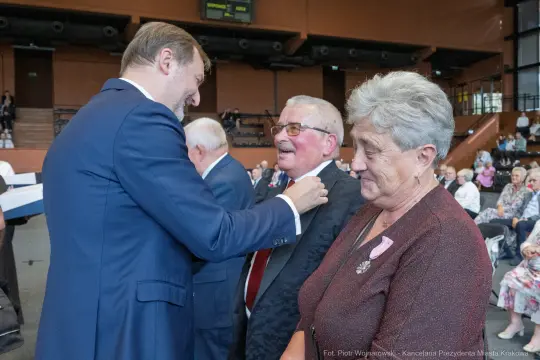 Uroczystość wręczenia odznaczeń, uśmiechnięte twarze, radosna atmosfera.