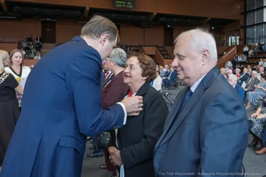 Spotkanie osób w formalnych strojach, rozmowa i uśmiechy w tle.