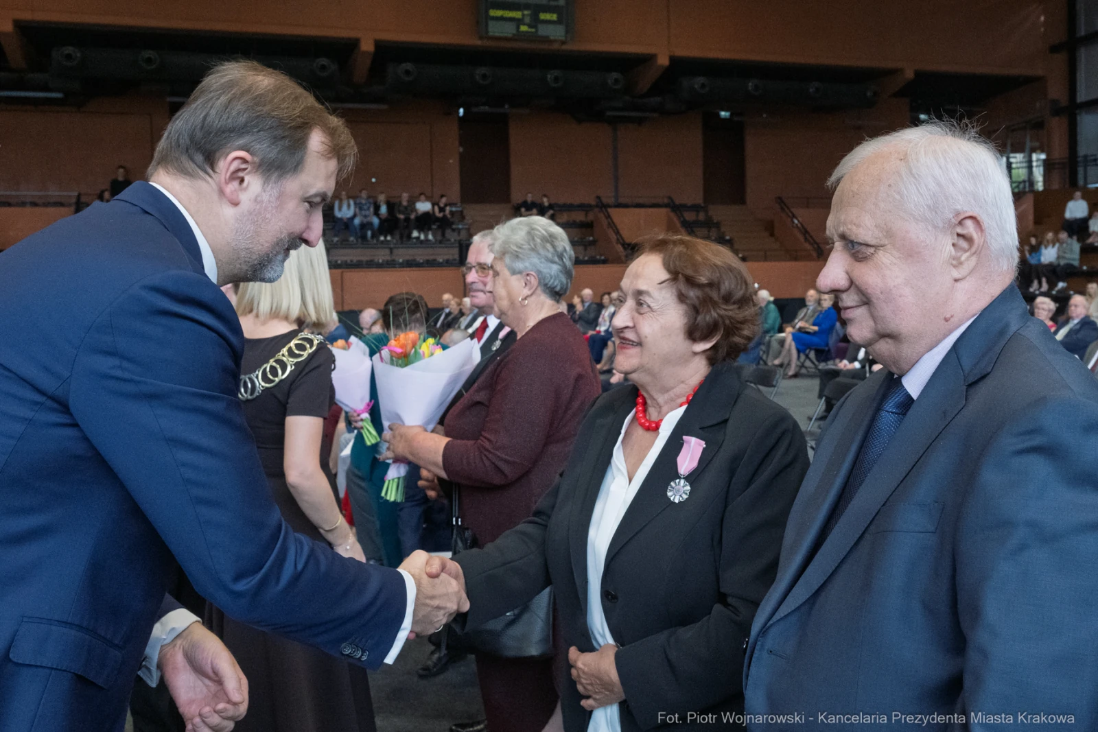 Uroczystość wręczenia odznaczeń, uściski dłoni i kwiaty w tle.  Autor: Piotr Wojnarowski