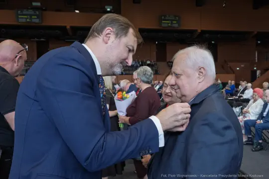 Mężczyzna przypina odznaczenie innemu mężczyźnie w trakcie uroczystości.