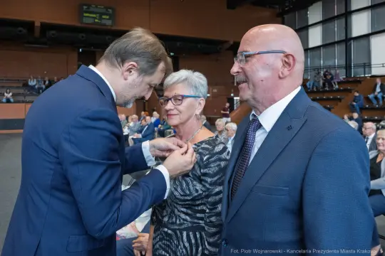 Wręczenie odznaczenia przez mężczyznę kobiecie w towarzystwie drugiego mężczyzny.