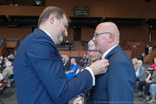 Uroczystość wręczenia odznaczeń, mężczyzna przypina medal innemu mężczyźnie.