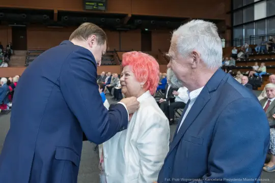 Wręczenie odznaczenia kobiecie przez mężczyznę w towarzystwie drugiego mężczyzny.