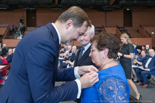 Uroczystość wręczenia odznaczeń, mężczyzna przypina medal kobiecie.