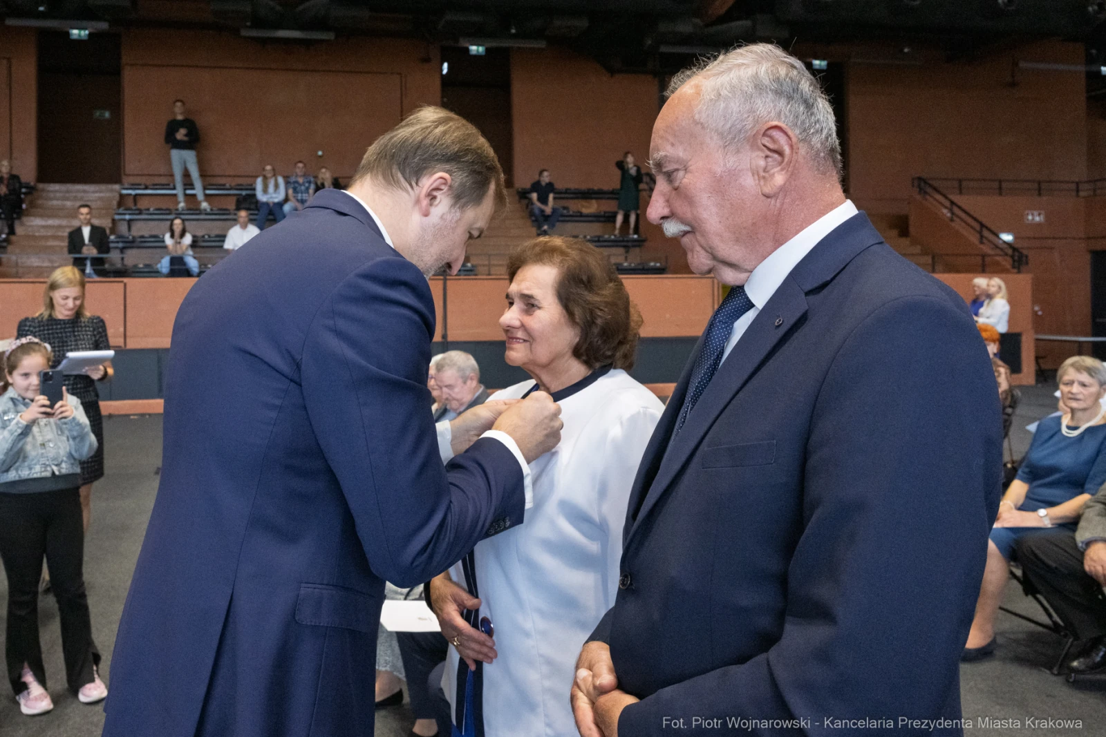 Wręczenie odznaczenia przez mężczyznę kobiecie w obecności innych osób.  Autor: Piotr Wojnarowski