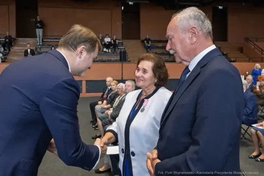Uroczystość wręczenia odznaczeń, uściski dłoni i uśmiechy uczestników.