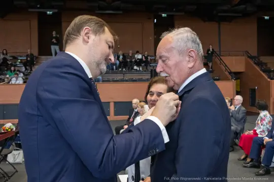 Uroczystość wręczenia odznaczeń, mężczyzna przypina medal do marynarki innego mężczyzny.