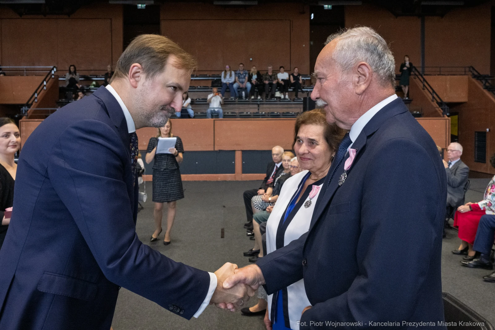 Uroczystość wręczenia odznaczeń, mężczyzna podaje rękę innemu mężczyźnie, w tle widownia.  Autor: Piotr Wojnarowski