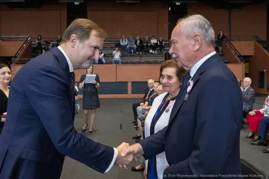 Uroczystość wręczenia odznaczeń, mężczyzna podaje rękę innemu mężczyźnie, w tle widownia.