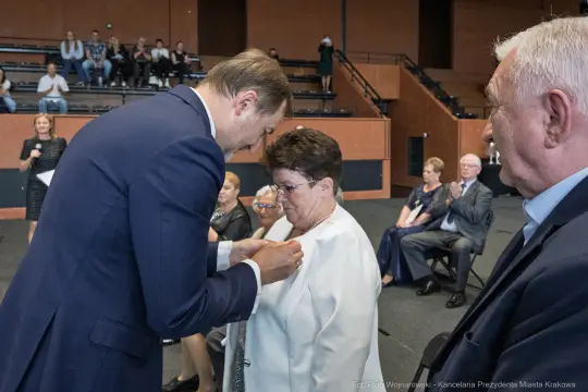 Wręczenie odznaczenia przez mężczyznę kobiecie w obecności zgromadzonych gości.