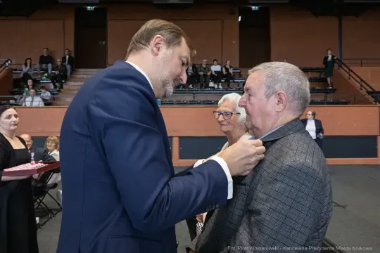 Wręczenie odznaczenia mężczyźnie w eleganckim garniturze podczas uroczystości.