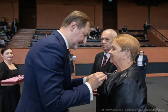 Wręczenie odznaczenia przez mężczyznę kobiecie w obecności innych osób.