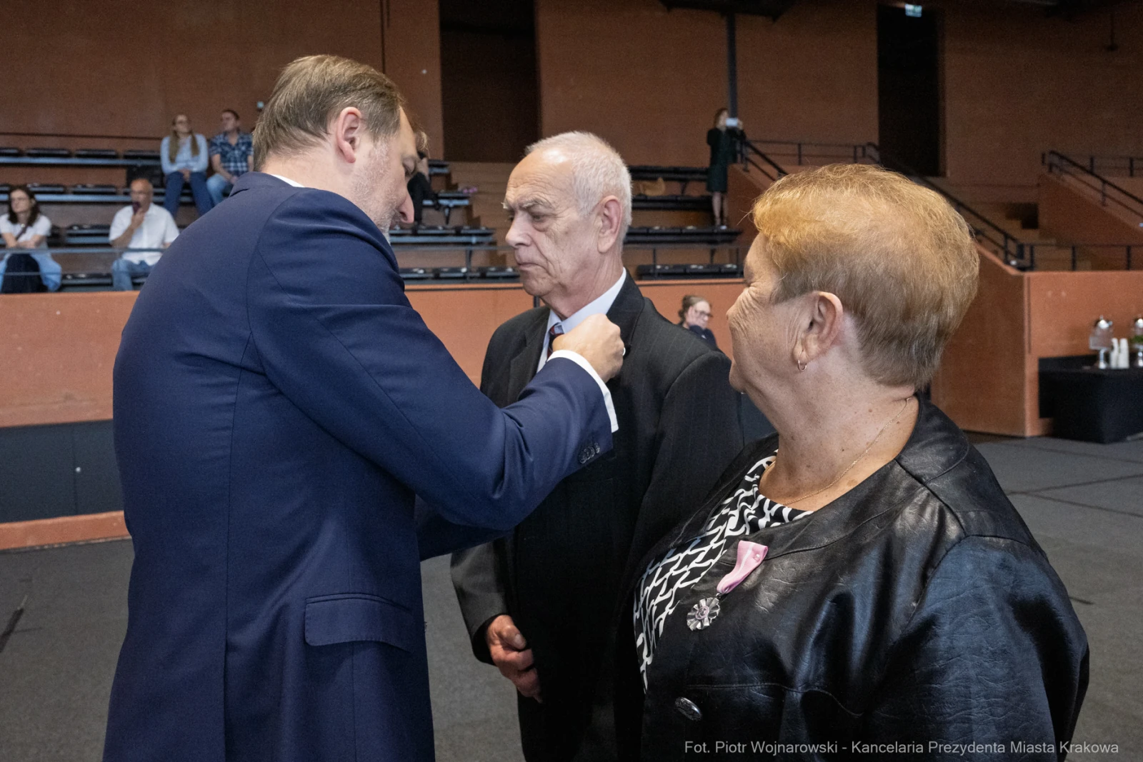 Ceremonia wręczenia odznaczeń, mężczyzna w garniturze rozmawia z odznaczonymi.  Autor: Piotr Wojnarowski