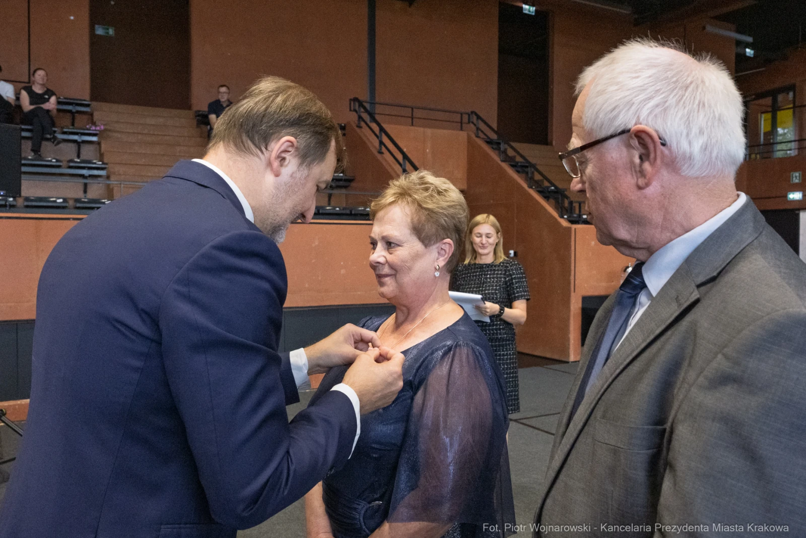 Wręczenie odznaczenia kobiecie przez mężczyznę w eleganckim otoczeniu.  Autor: Piotr Wojnarowski