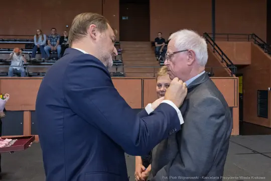 Wręczenie odznaczenia mężczyźnie w garniturze podczas uroczystości.