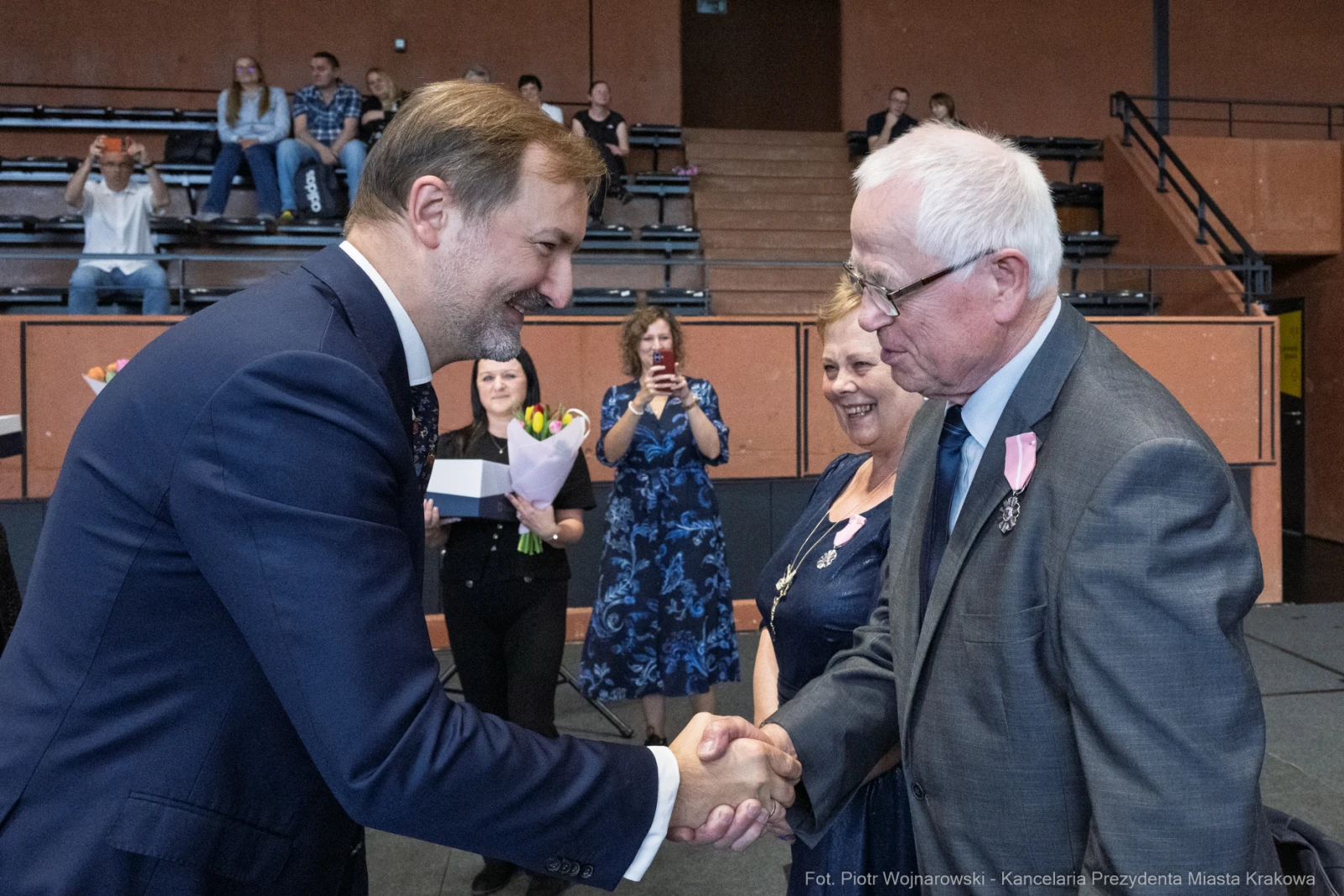 Uścisk dłoni dwóch mężczyzn podczas uroczystości, w tle goście z kwiatami.  Autor: Piotr Wojnarowski
