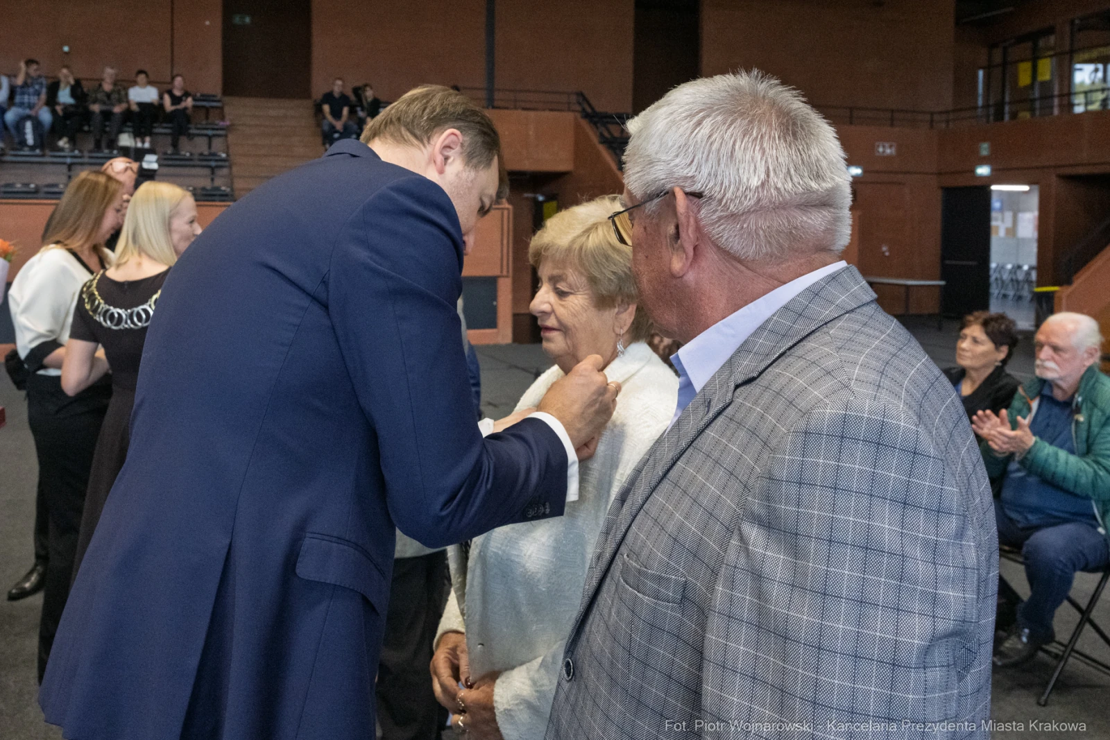 Wręczenie odznaczenia przez mężczyznę starszej kobiecie w obecności innych gości.  Autor: Piotr Wojnarowski
