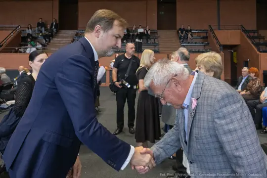 Uścisk dłoni między dwoma mężczyznami podczas uroczystości. W tle zgromadzeni goście.