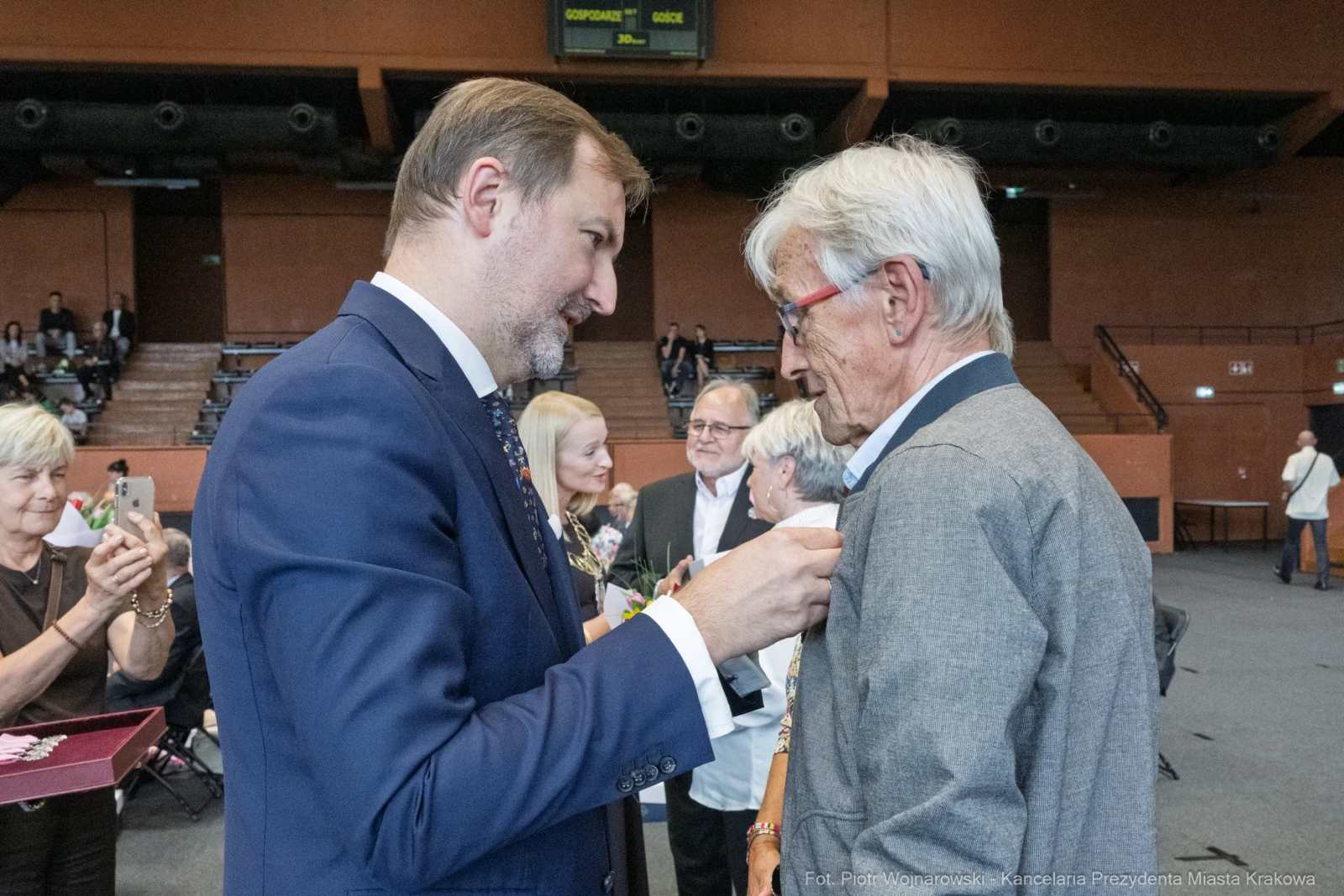Wręczenie odznaczenia przez mężczyznę w garniturze starszemu mężczyźnie w okularach.  Autor: Piotr Wojnarowski