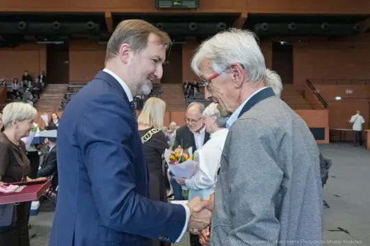 Uroczystość wręczenia nagród, mężczyźni w garniturach wymieniają uściski dłoni.