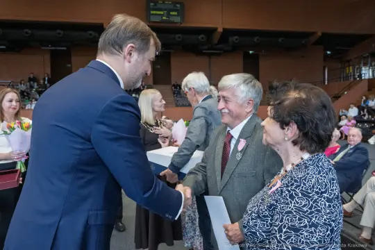 Uroczystość wręczenia nagród, uściski dłoni i kwiaty w tle.