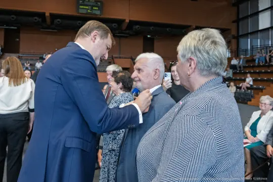 Uroczystość wręczenia odznaczeń, mężczyzna przypina medal do marynarki innego mężczyzny.