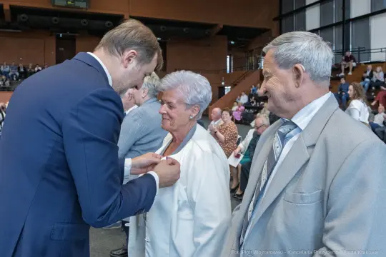 Uroczystość wręczenia odznaczeń, osoby w eleganckich strojach, emocjonalne chwile.