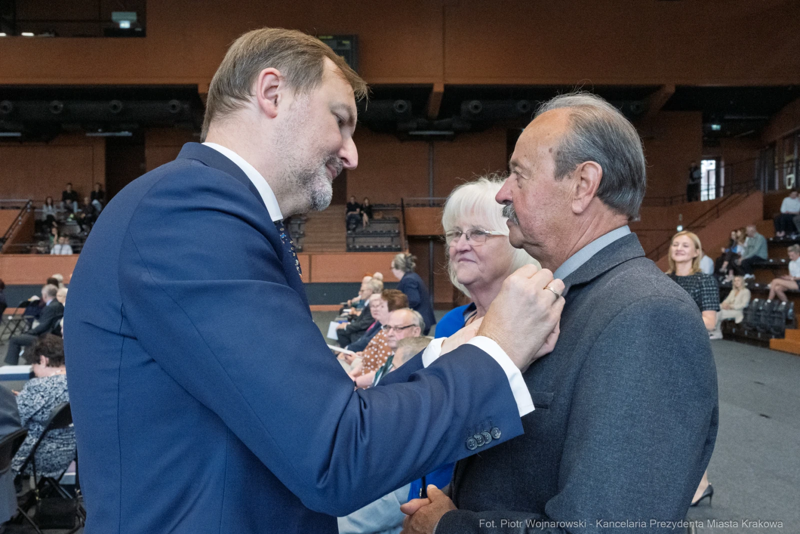 Mężczyzna poprawia krawat innego mężczyzny, w tle widoczni uczestnicy wydarzenia.  Autor: Piotr Wojnarowski
