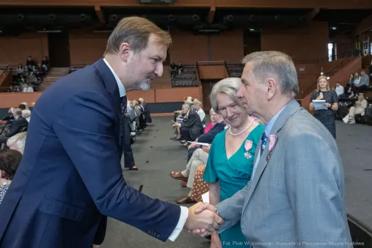 Uścisk dłoni między mężczyzną a starszym mężczyzną, w tle siedzący goście.