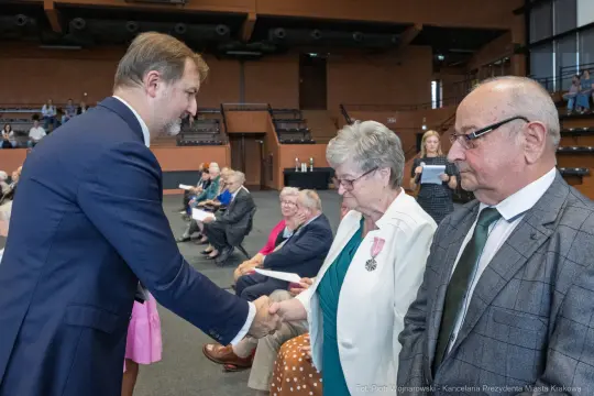 Uroczystość wręczenia odznaczeń, uściski dłoni i wzruszone twarze uczestników.