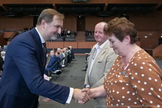 Uścisk dłoni między mężczyzną a kobietą, w tle siedzący ludzie.
