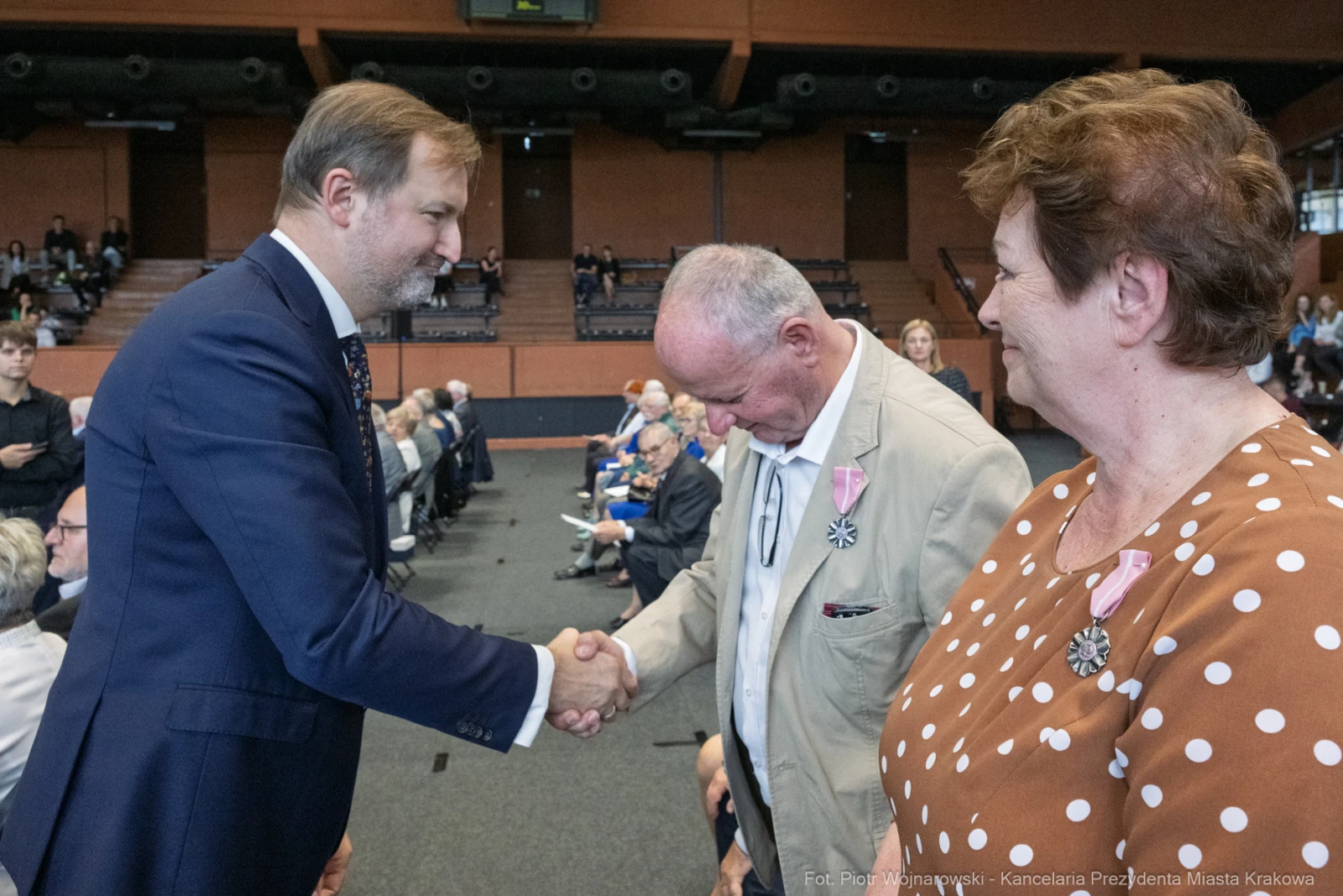 Uścisk dłoni między mężczyzną a osobą w garniturze, w tle widownia.  Autor: Piotr Wojnarowski