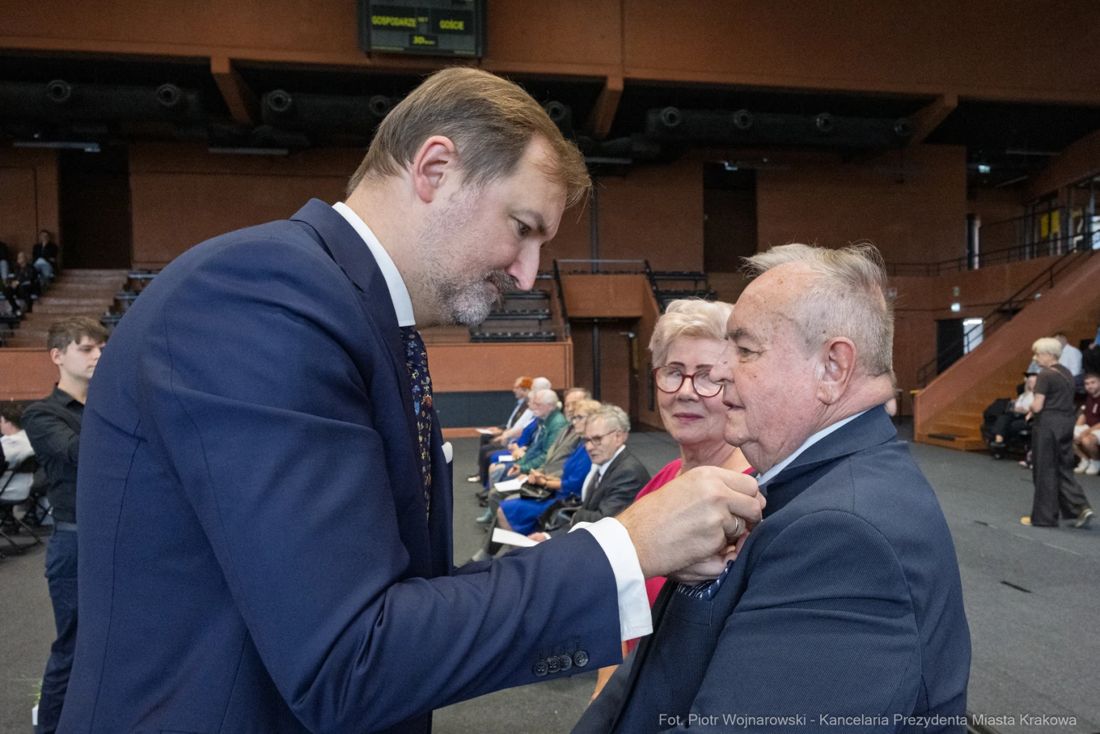 Wręczenie odznaczenia mężczyźnie przez elegancko ubranego mężczyznę w towarzystwie starszej pary.  Autor: Piotr Wojnarowski