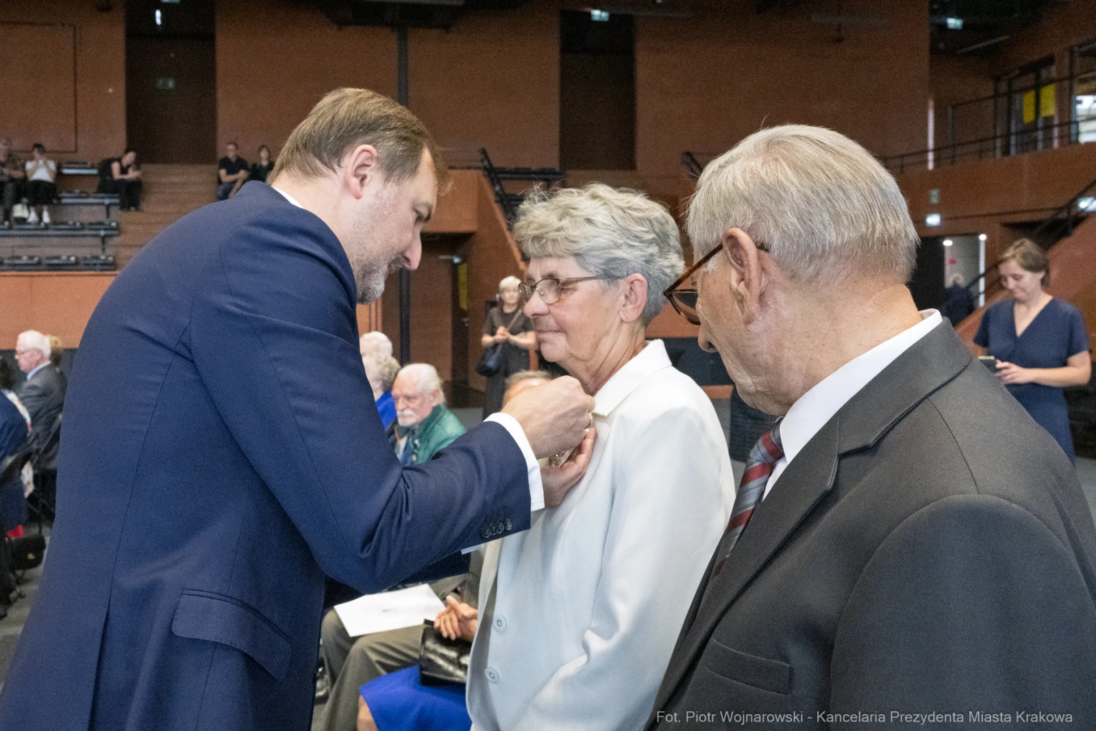 Uroczystość wręczenia odznaczeń, osoby w formalnych strojach, moment przypinania odznaki.  Autor: Piotr Wojnarowski