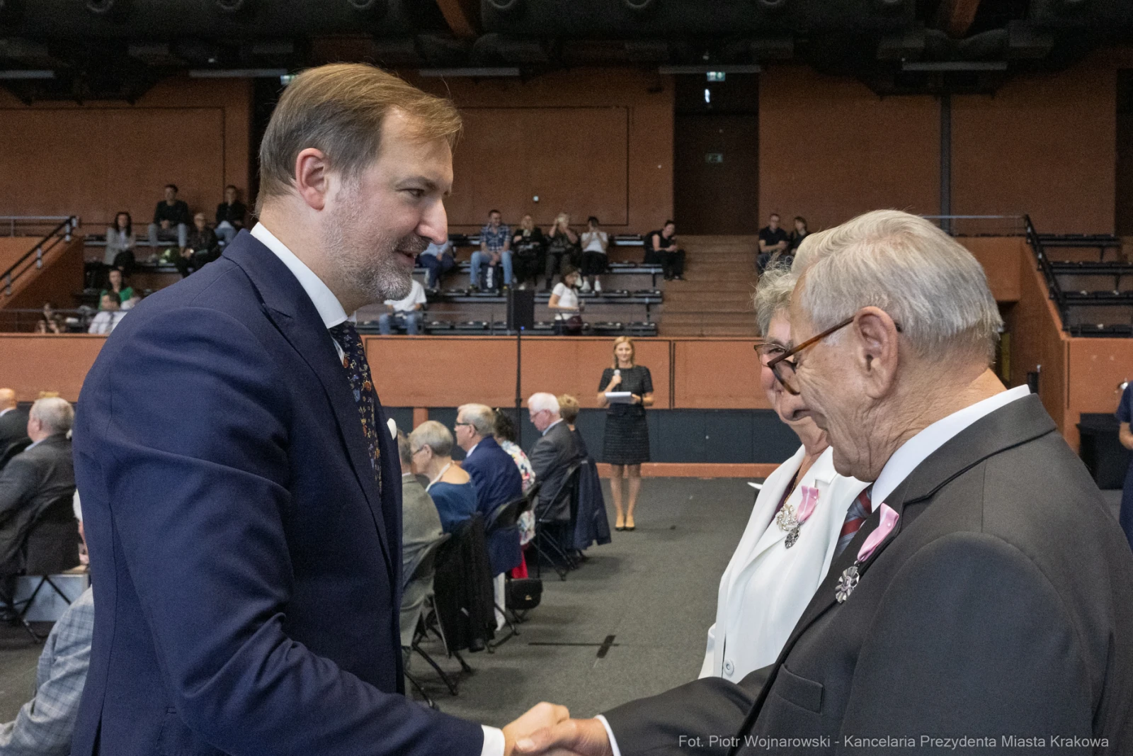 Uścisk dłoni między mężczyzną a starszym panem, w tle widoczna grupa ludzi.  Autor: Piotr Wojnarowski